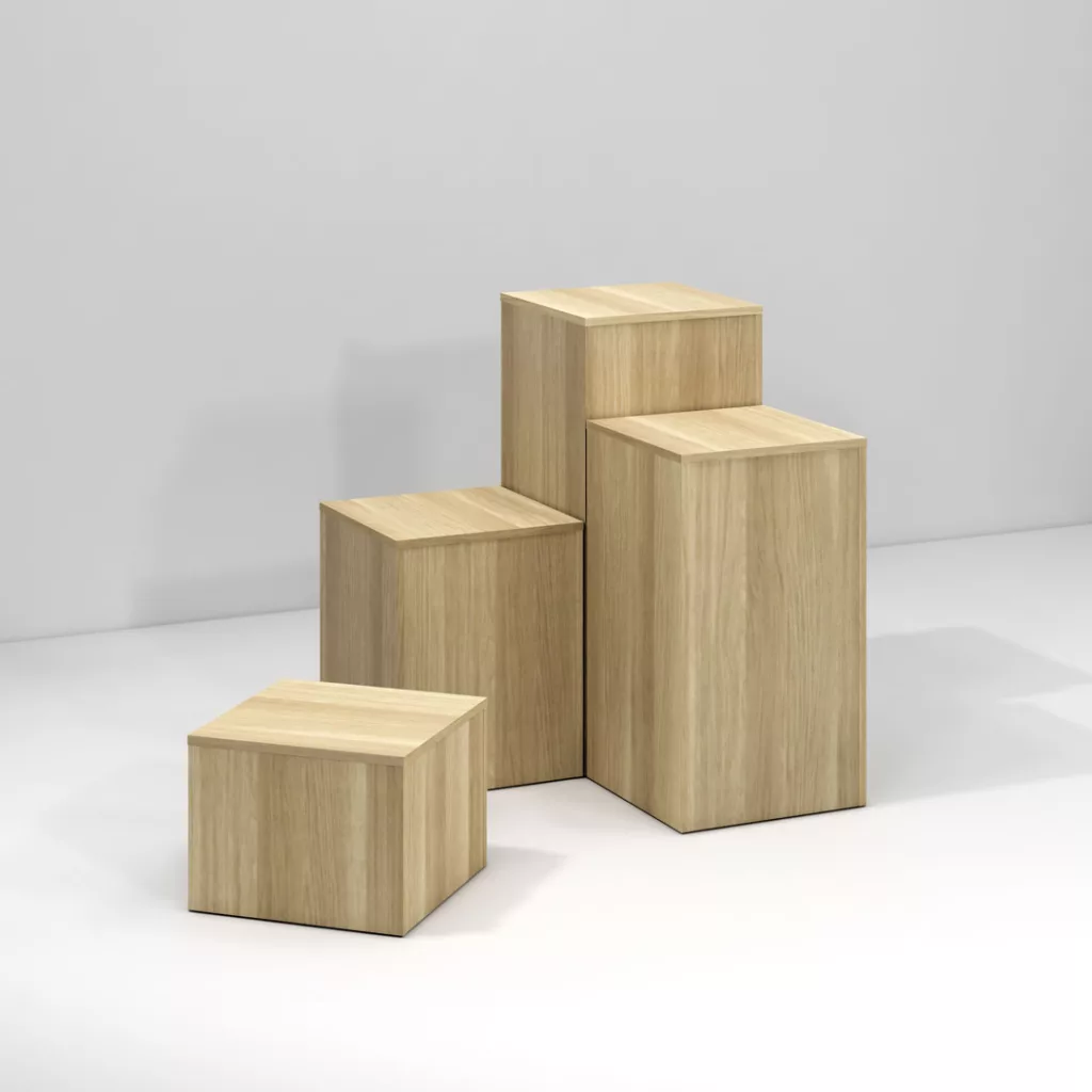 Four wooden pedestals of varying heights and sizes are arranged in a group on a white background. They feature a light wood grain texture and a simple, cubic design, offering versatile shopfitting solutions for any display needs.
