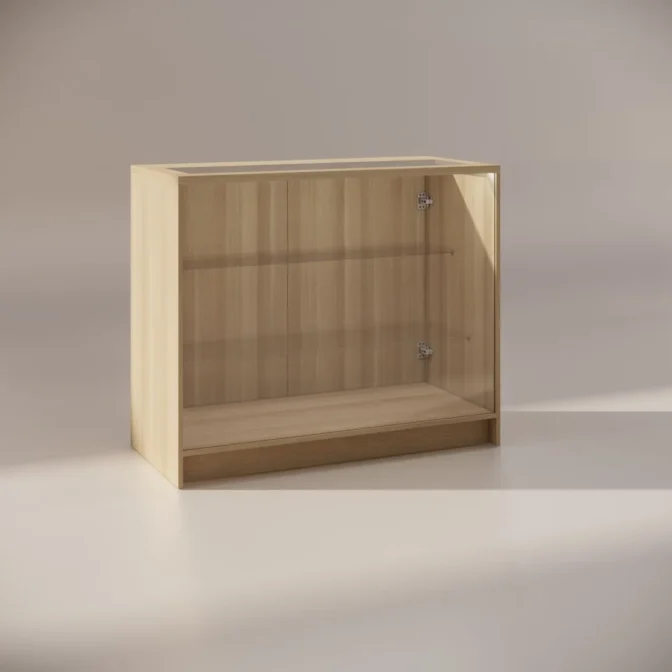 A wooden display cabinet with a clear glass front and sides, featuring a single shelf inside. The cabinet stands on a smooth surface and is illuminated by soft lighting from the left.