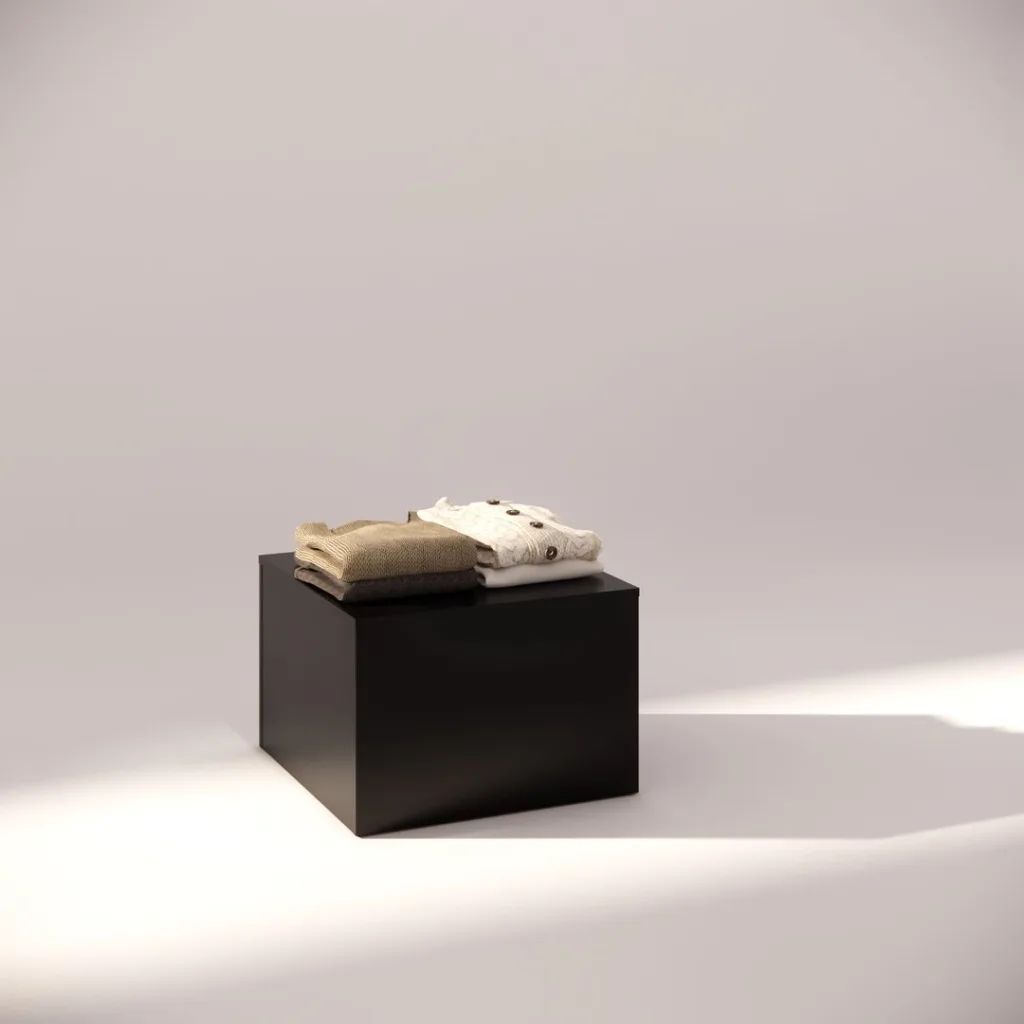 A folded brown sweater and a white polka dot sweater are elegantly arranged on a Black Small Square Display Pedestal 400mm, set against a soft, neutral background with gentle lighting.