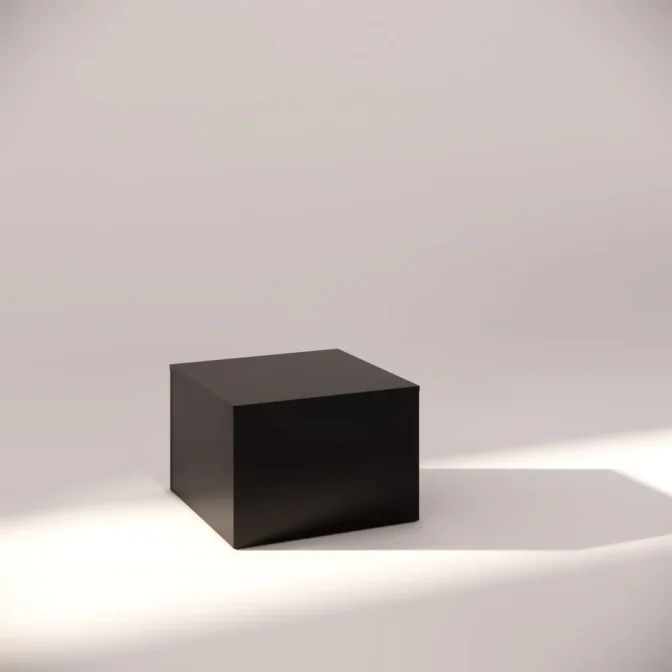 A black cube sits on a light-colored surface with soft shadows around it, highlighted by gentle lighting from the side, creating a minimalist and modern appearance.