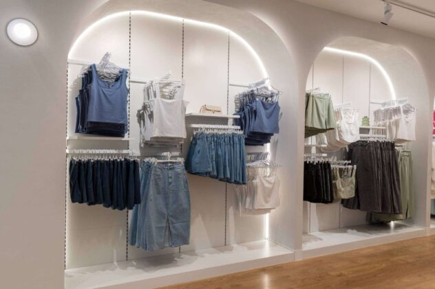 A clothing display in a store showcases various women's apparel on hangers, including tank tops, skirts, and pants. The outfits are organized by color and style in a well-lit, minimalist setting that highlights the items - a perfect example of effective brand partnerships at work.