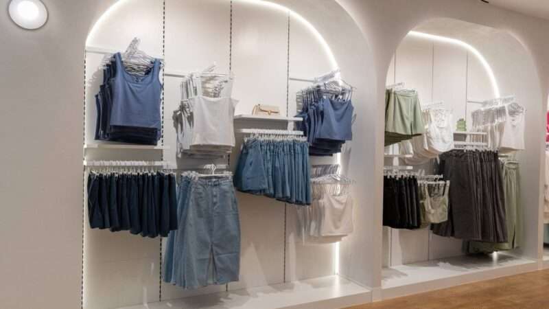 A clothing display in a store showcases various women's apparel on hangers, including tank tops, skirts, and pants. The outfits are organized by color and style in a well-lit, minimalist setting that highlights the items - a perfect example of effective brand partnerships at work.