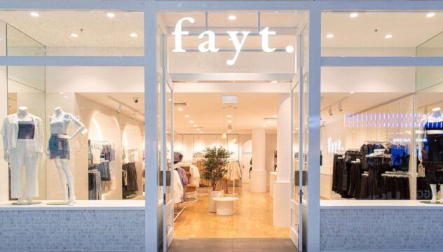 Storefront of a fashion boutique named fayt, showcasing brand partnerships with mannequins dressed in stylish outfits. The well-lit interior features clothing racks and a central plant display. Wooden flooring adds warmth to the decor, highlighting fayt's commitment to exclusive collaborations.