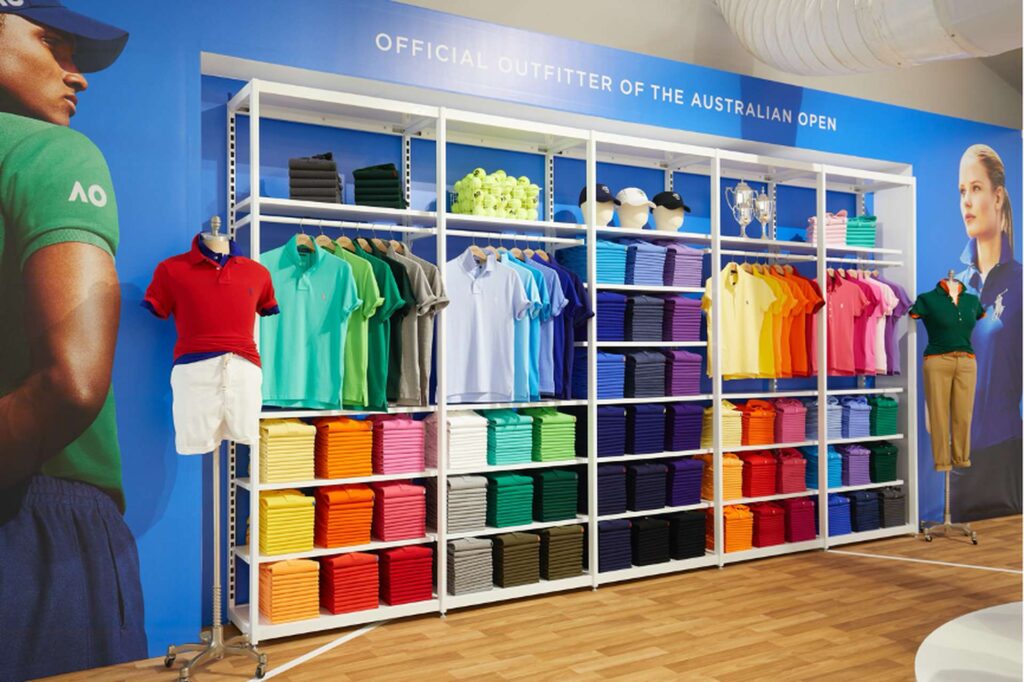 A retail display features colorful polo shirts and tennis attire, neatly stacked on shelves. Mannequins showcase outfits alongside banners with tennis players, highlighting brand partnerships for the Australian Open. The setting is bright and organized, capturing the excitement of the event.