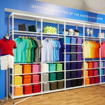 A retail display features colorful polo shirts and tennis attire, neatly stacked on shelves. Mannequins showcase outfits alongside banners with tennis players, highlighting brand partnerships for the Australian Open. The setting is bright and organized, capturing the excitement of the event.