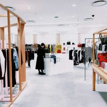 A modern clothing store with thoughtfully merchandised garments on racks, shelves, and display table. A person is browsing clothes at a central display, succumbing to impulse buying. The store boasts a minimalist design with neutral colors and soft lighting.